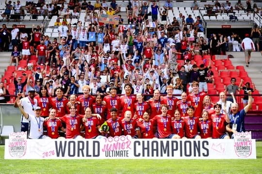 The U.S. U-20 team with their gold medals in front of the stands, behind a World Junior Ultimate Champions 2026 banner.